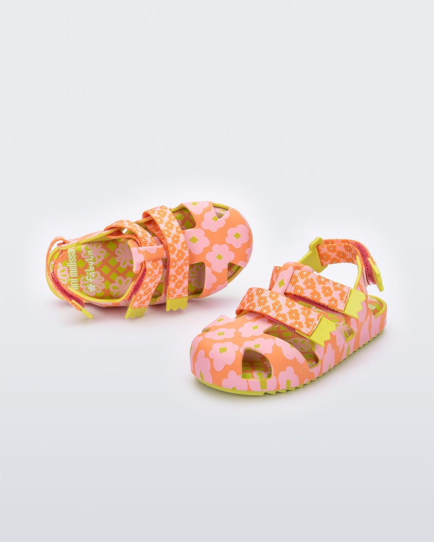 An angled front and top view of a pair of Yellow/Orange Mini Melissa Yoyo sandals with orange and pink floral base, 2 front velcro straps, 1 back velcro strap and a yellow sole.