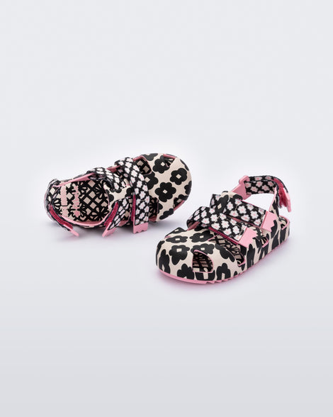 An angled front and top view of a pair of pink/black sandals Mini Melissa Yoyo with a pink and black floral base, two velcro front straps and a back ankle strap.