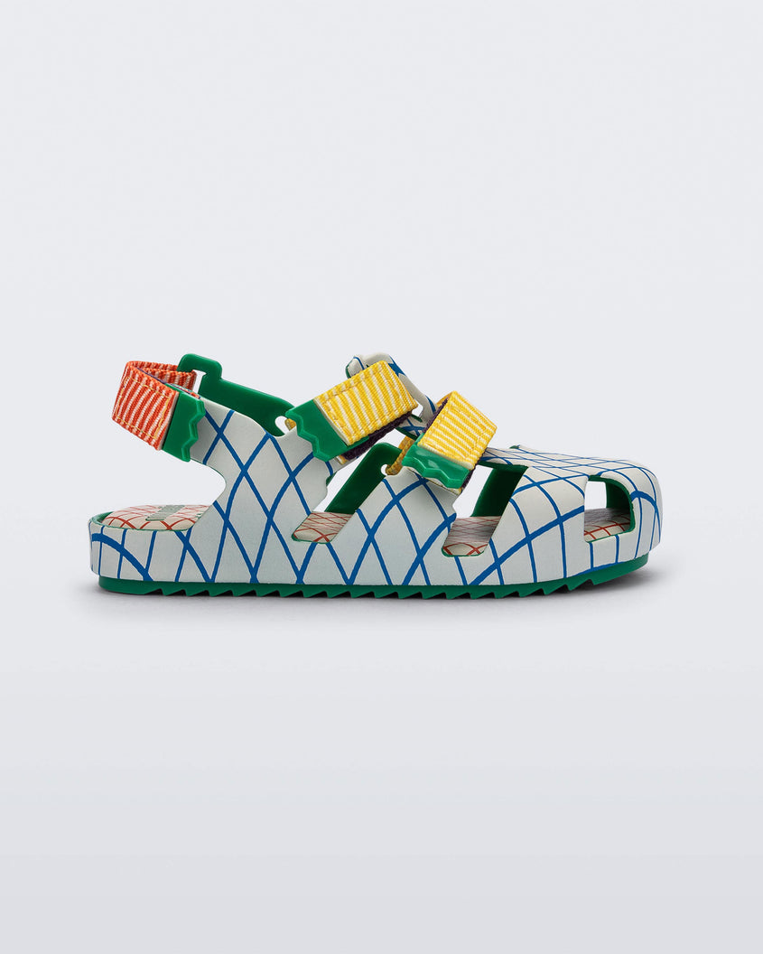 Side view of a green/beige Mini Melissa Yoyo sandal with a gray, green and blue patterned base, with two yellow velcro front straps and a red ankle strap.
