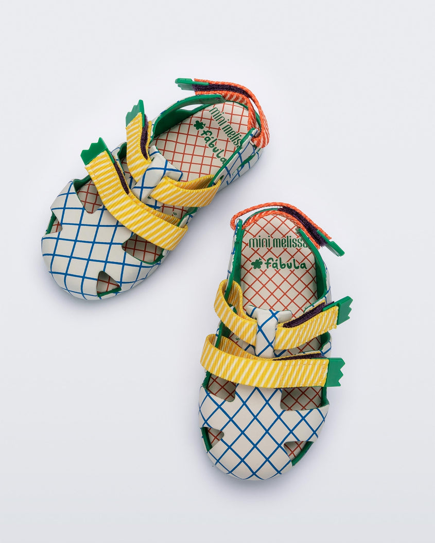Top view of a pair of green/beige Mini Melissa Yoyo sandals with a gray, green and blue patterned base, with two green and yellow velcro front straps and a red and green ankle strap.