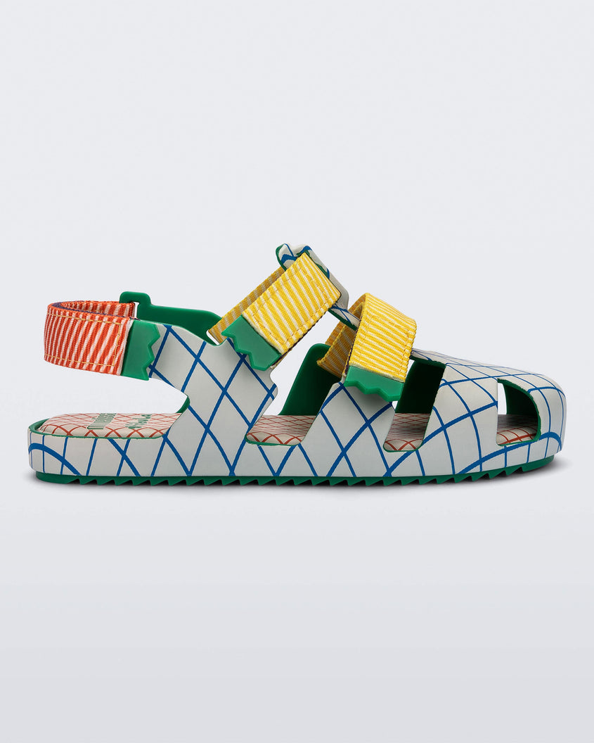 Side view of a Green/Beige Mini Melissa Yoyo sandal with a gray/blue patterned base with two front yellow and green velcro straps and a red and green ankle strap.