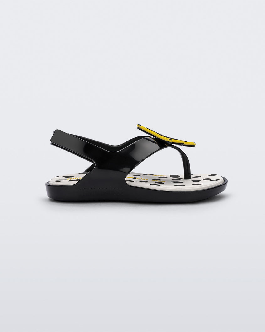 Side view of a black Mini Melissa Sunny sandal with a black base, a banana drawing on top of the straps and a black and white polka dot insole.