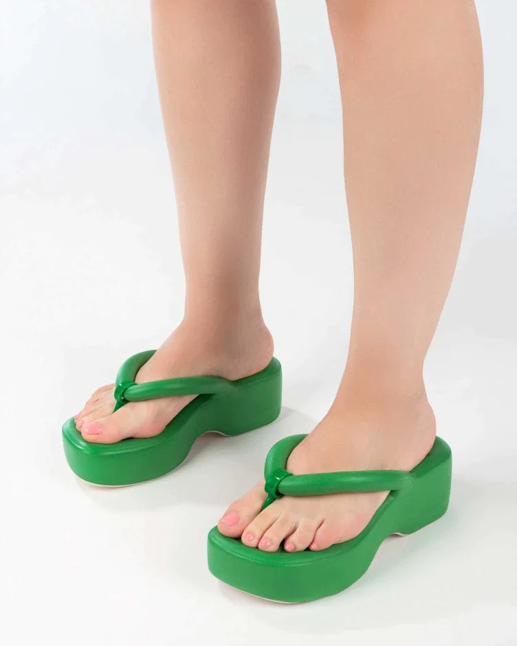 A model's legs wearing a pair of green Melissa Free Platform Flip Flops with puffer-like straps.