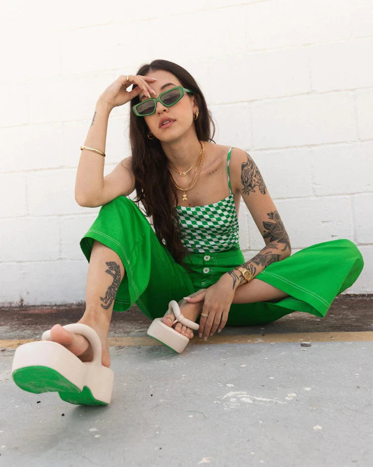 A model posing for a picture, sitting on the ground, wearing green pants and a pair of beige Melissa Free Platform Flip Flops with puffer-like straps.