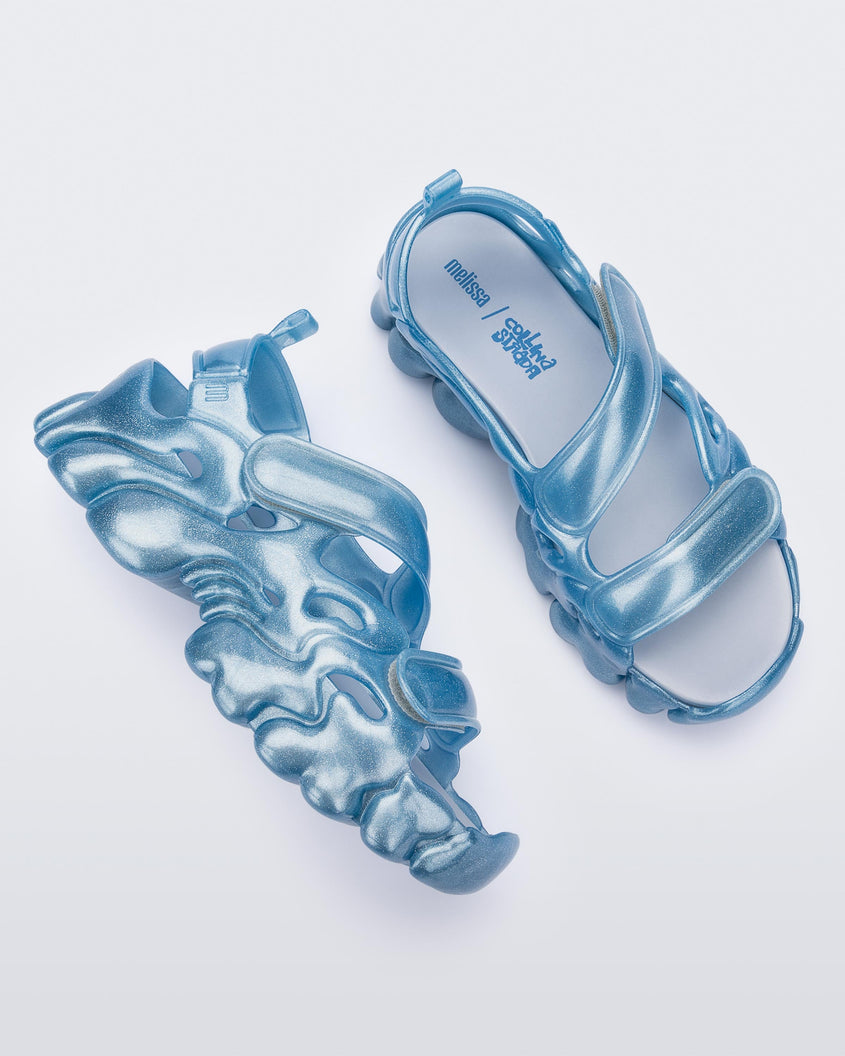 Top and side view of a pair of Melissa Puff chunky sandals in glitter blue with velcro straps
