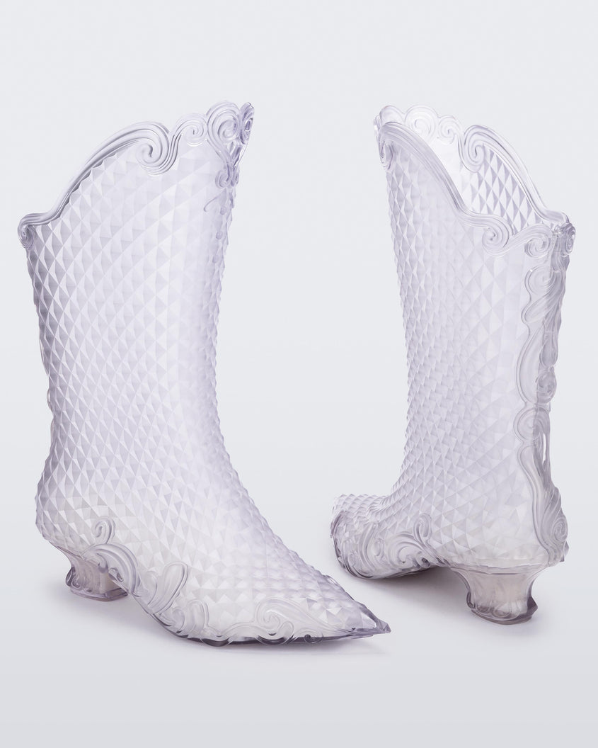 An angled front and back view of a pair of transparent glass looking Melissa Court Boots with a short heel, heart detail on the front and a checkered pattern texture.
