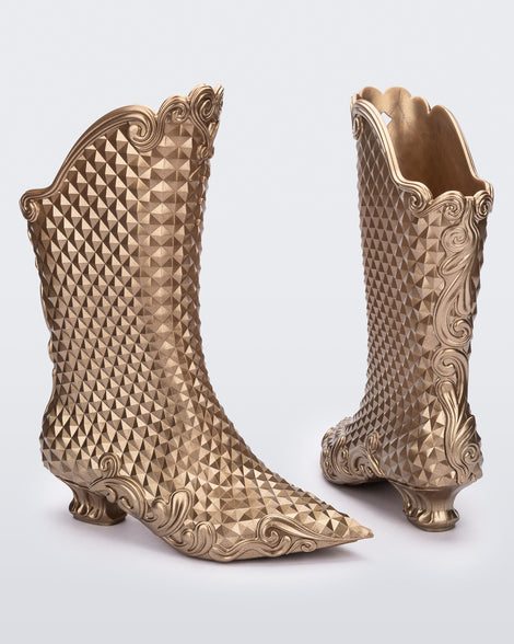 An angled back and side view of a pair of metallic gold Melissa Court Boots with a short heel, heart detail on the front and a checkered pattern texture.