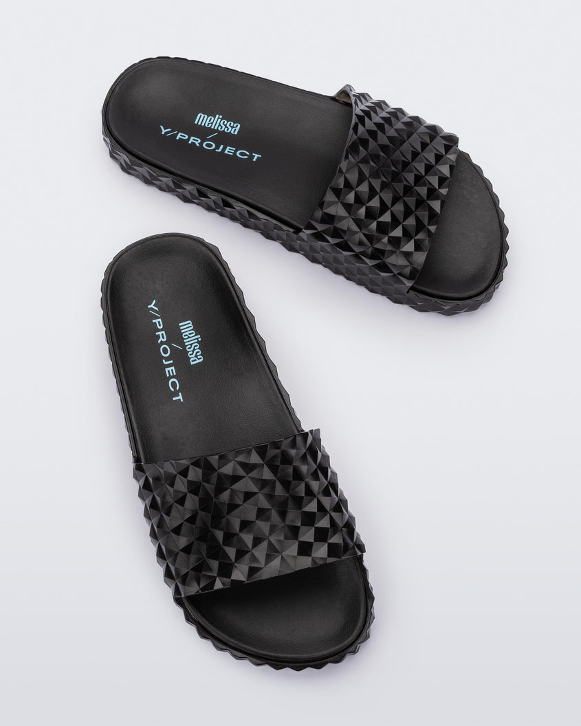 Top view of a pair of black Melissa Court Slides with a checkered pattern texture.