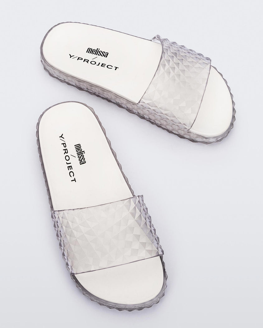A top view of a pair of transparent clear/white Melissa Court Slides with a checkered pattern texture.