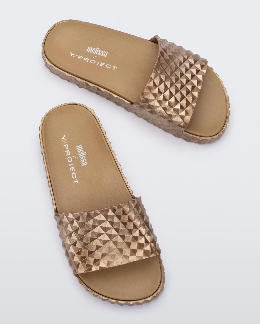 Top view of a pair of gold Melissa Court Slides with a checkered pattern texture.