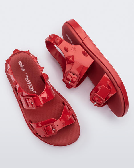 A top and side view of a pair of red Melissa Spikes Sandals with two straps with buckles on top and spike details around the base.