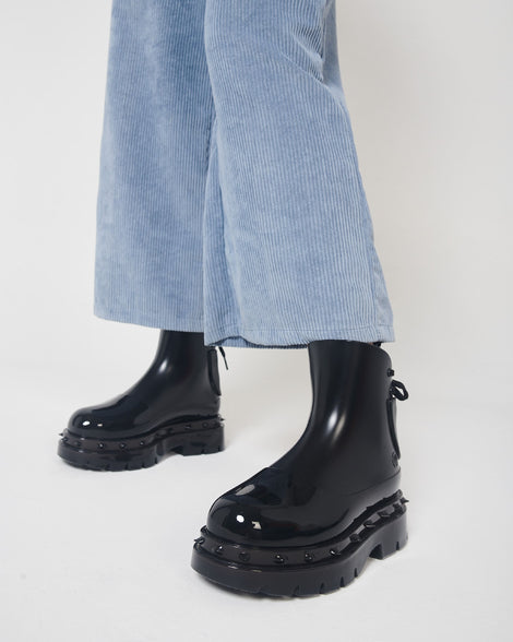 A model's legs in blue corduroy pants and a pair of black Melissa Spikes Boots with spike details around the sole and laces in the back.