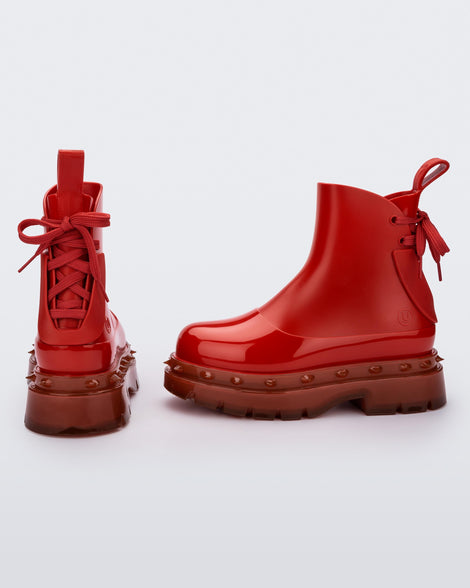 An angled side and top view of a pair of red Melissa Spikes Boots with spike details around the sole and laces in the back.