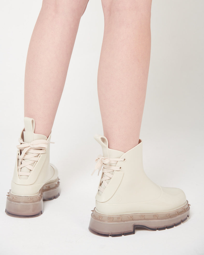 A model's legs wearing a pair of beige Melissa Spikes Boots with spike details around the sole and laces in the back.