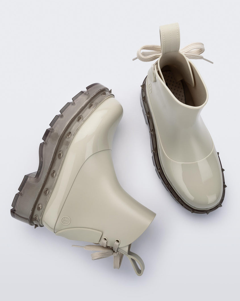 A top and side view of a pair of beige Melissa Spikes Boots with spike details around the sole and laces in the back.
