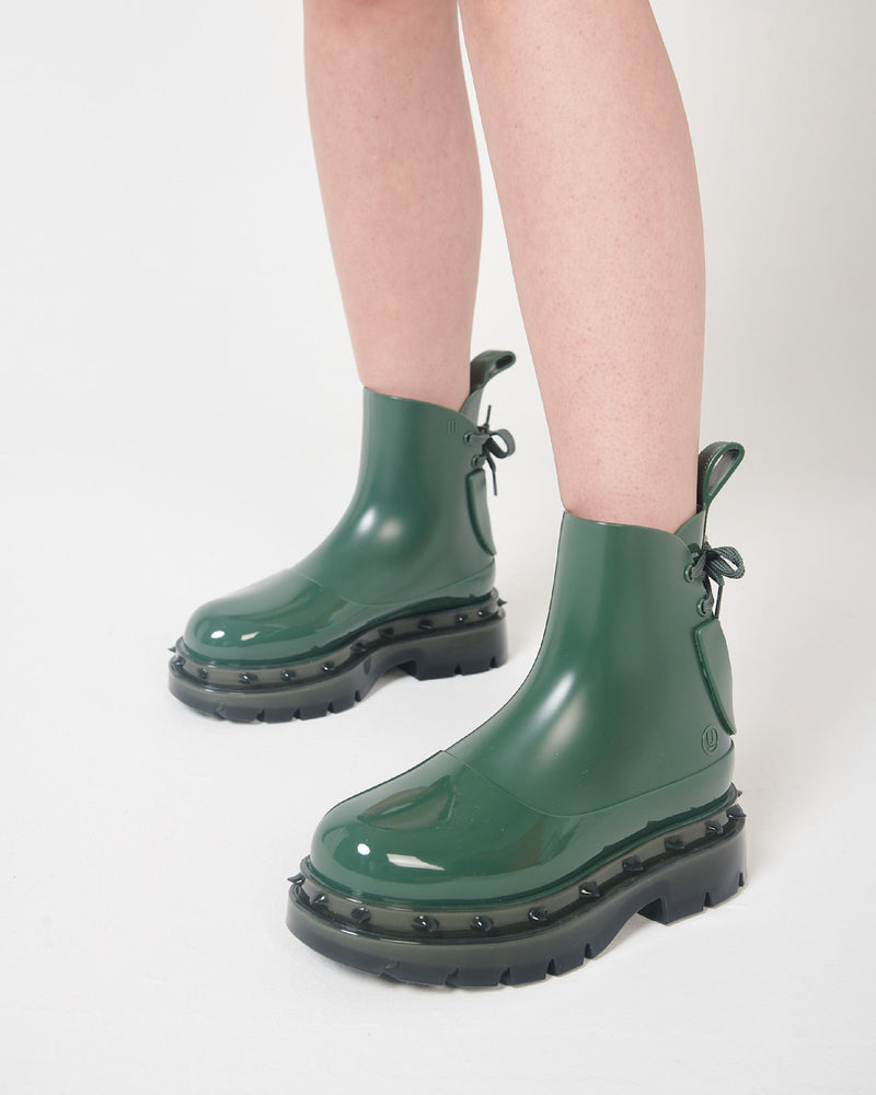 A model's legs wearing a pair of green Melissa Spikes Boots with spike details around the sole and laces in the back.