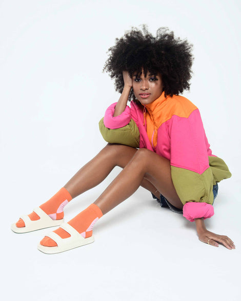 A model posing for a picture, sitting on the ground with her legs crossed wearing a pair of beige Melissa Free Grow slides with a square cut out on the front.