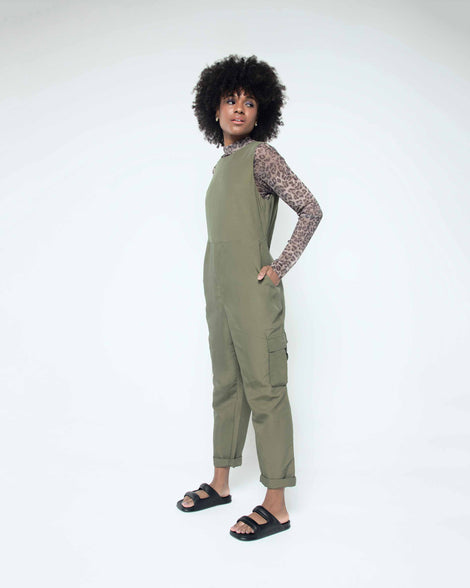 A model posing for a picture in a green jumpsuit and a pair of black Melissa Free Grow slides with a square cut out on the front.