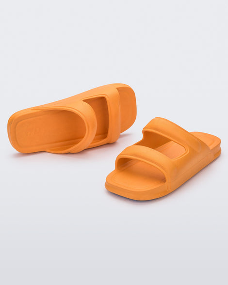An angled front and side view of a pair of orange Melissa Free Grow slides with a square cut out on the front.
