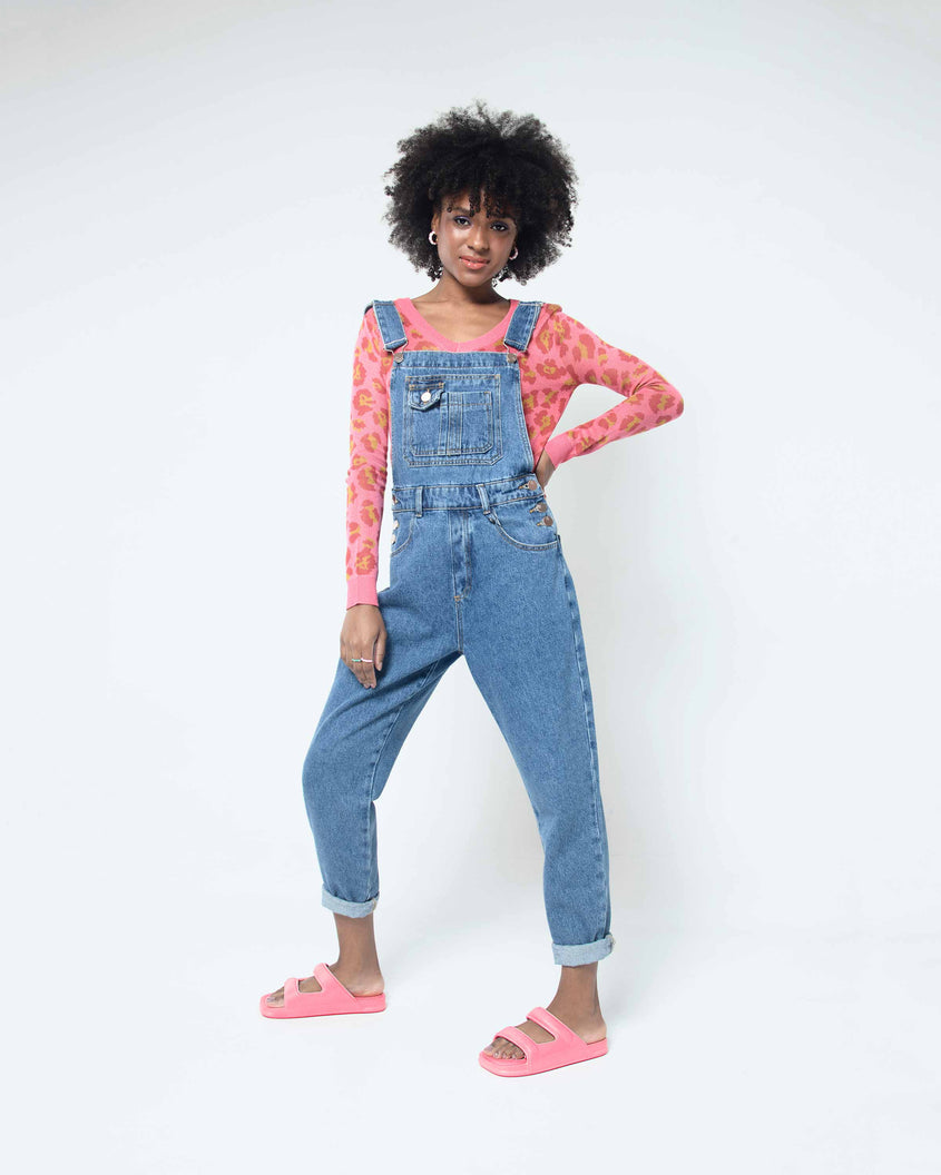 A model posing for a picture in overalls wearing a pair of pink Melissa Free Grow slides with a square cut out on the front.