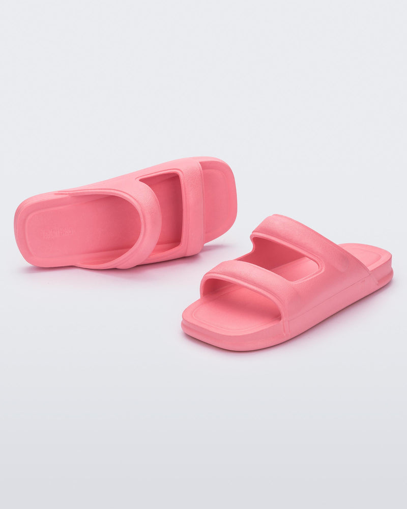 An angled front and side view of a pair of pink Melissa Free Grow slides with a square cut out on the front.