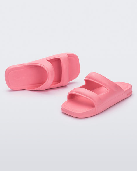 An angled front and side view of a pair of pink Melissa Free Grow slides with a square cut out on the front.
