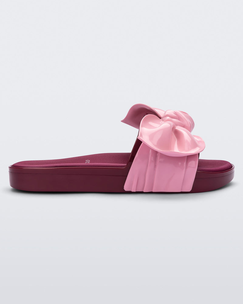 Side view of a of red/pink Melissa Tie Beach slide with a red base and a pink bow on the front strap.