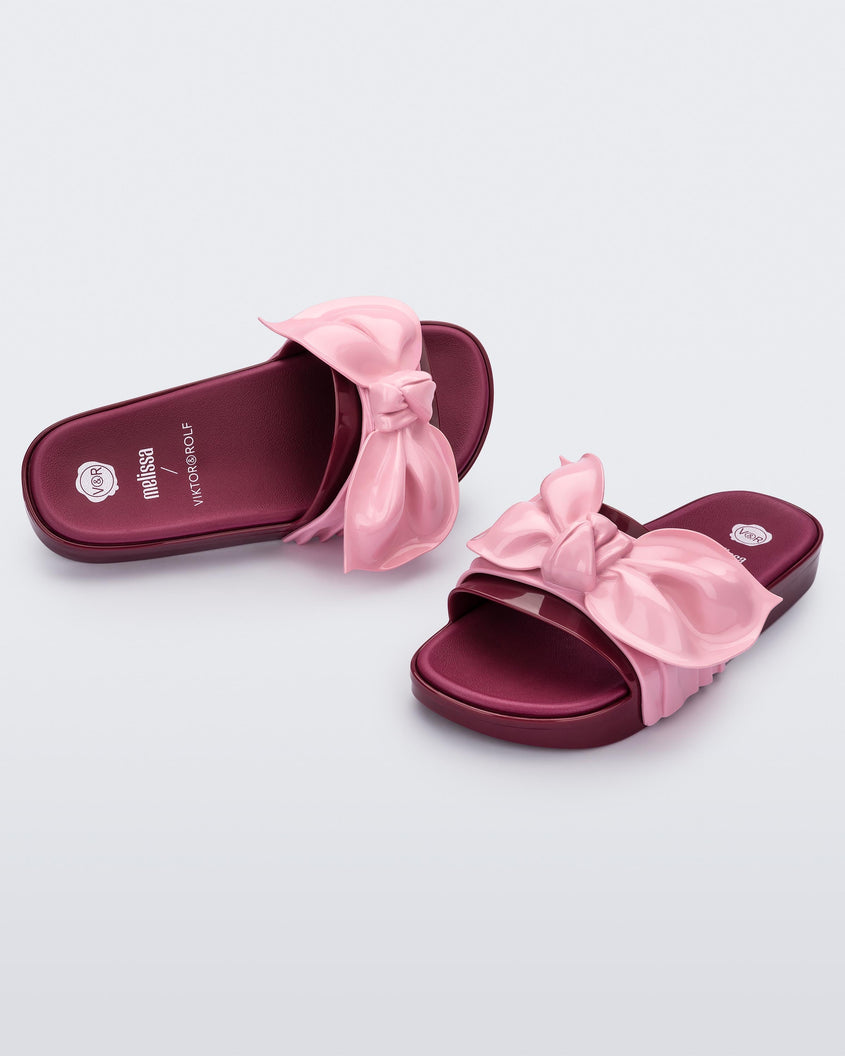 Angled front and top view of a pair of red/pink Melissa Tie Beach slides with a red base and a pink bow on the front strap.