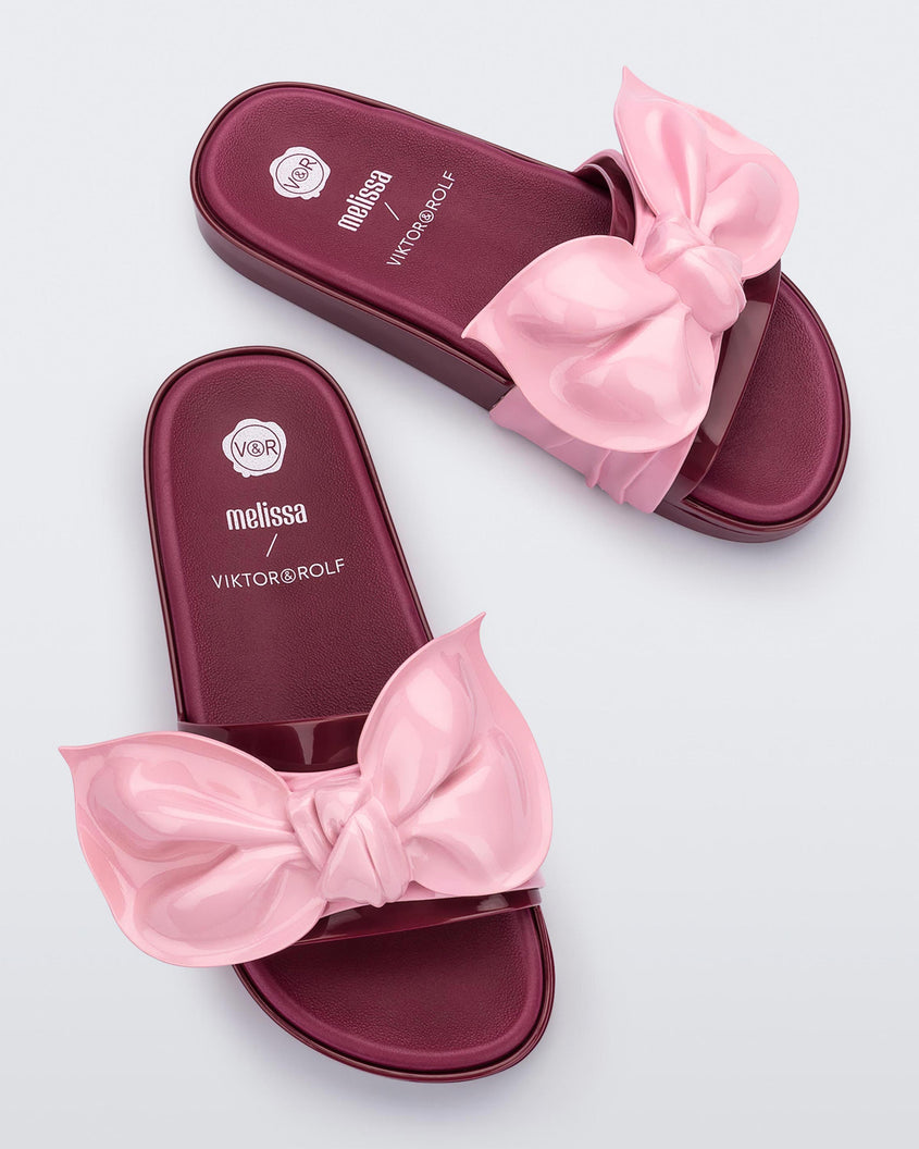 A top view of a pair of red/pink Melissa Tie Beach slides with a red base and a pink bow on the front strap.