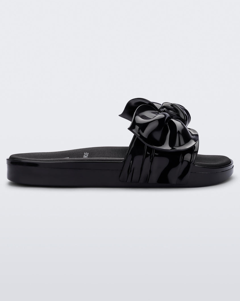 Side view of a black Melissa Tie Beach slide with a black base and a bow on the front strap.