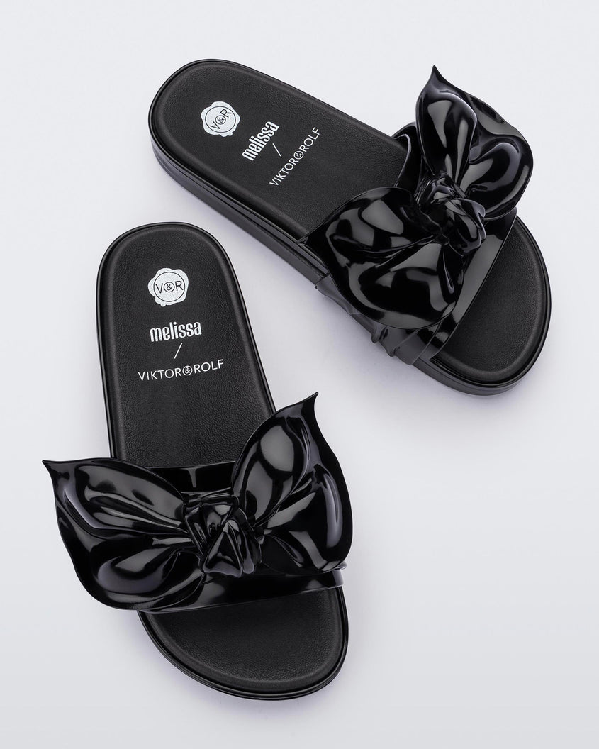 A top view of a pair of black Melissa Tie Beach slides with a black base and a bow on the front strap.