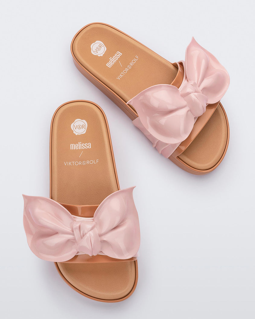 Top view of a pair of beige/pink Melissa Tie Beach slides with a beige base and a pink bow on the top strap.