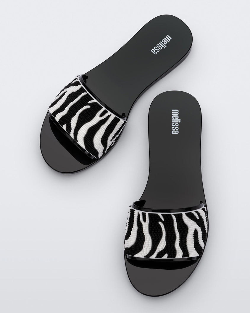Top view of a pair of black/white Melissa Savage slides with a zebra print on the strap.