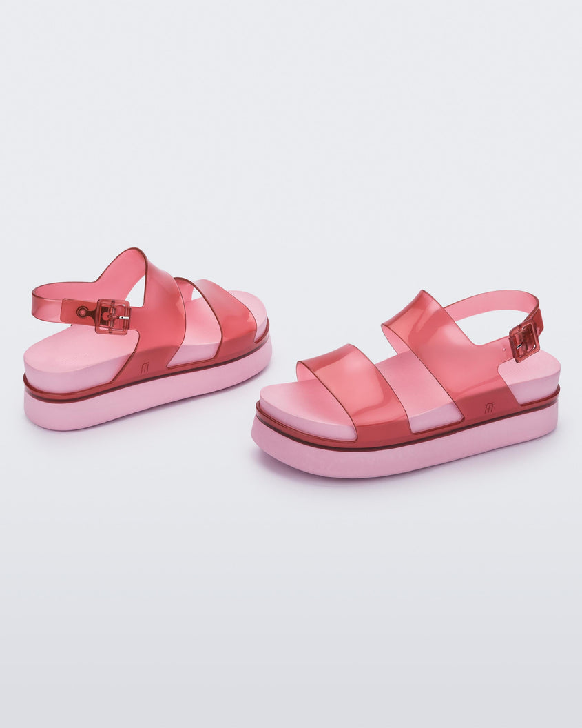 A side view of a pair of transparent red/pink Melissa Cosmic platform sandals with a pink sole and two red straps.