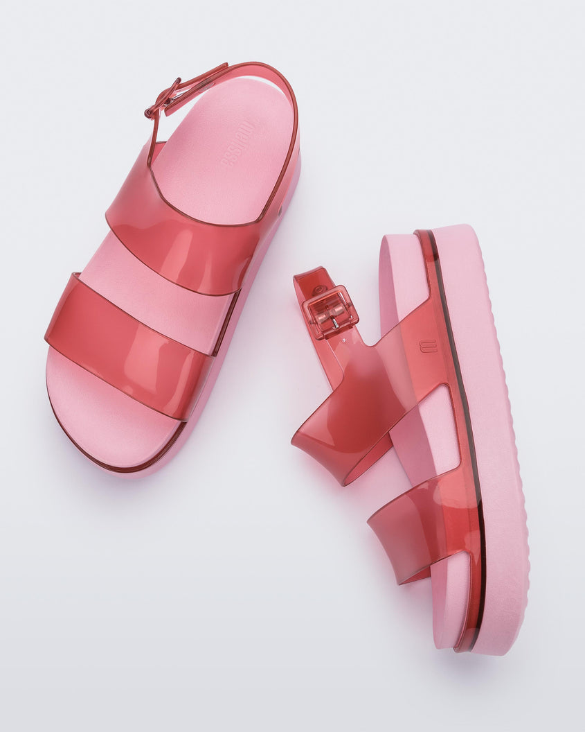 A top and side view of a pair of transparent red/pink Melissa Cosmic platform sandals with a pink sole and two red straps.