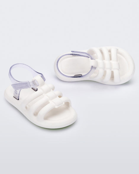 An angled front and side view of a pair of white Mini Melissa Freesherman sandals with white and clear glitter straps.