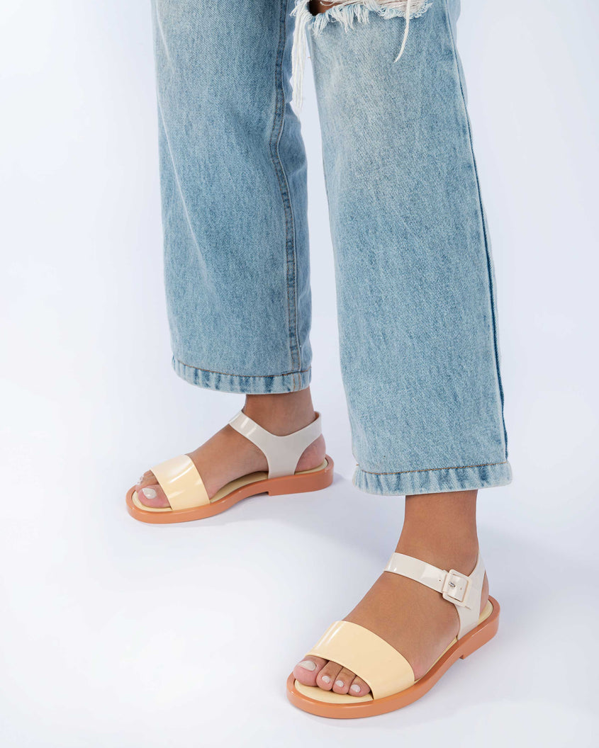 A model's legs wearing jeans and a pair of woman wearing a pair of beige/yellow Melissa Mar Sandal with two straps.