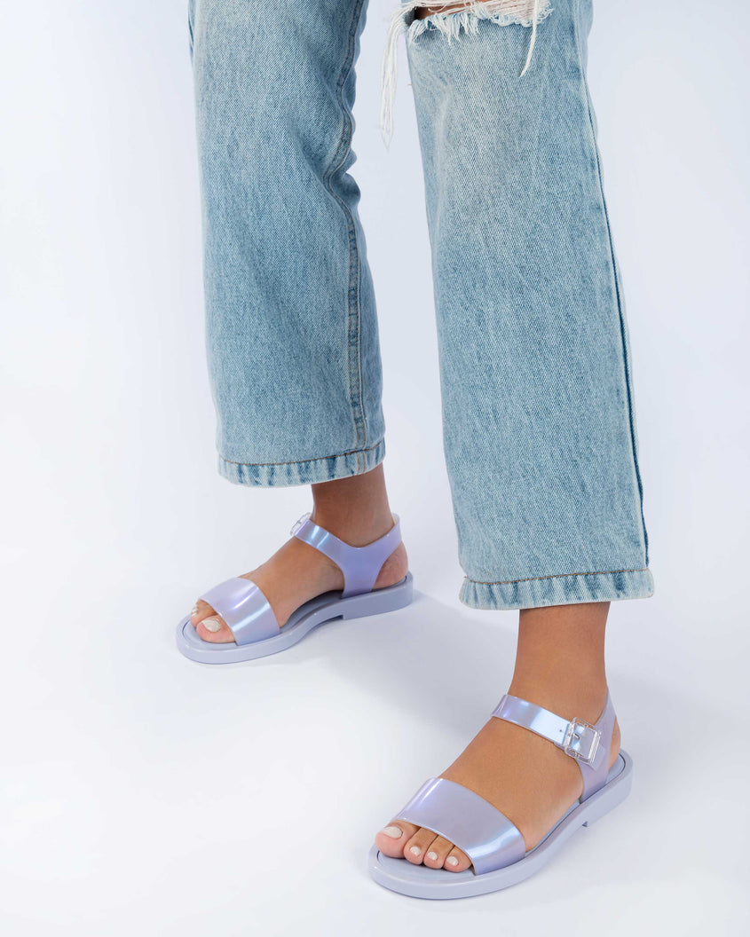 A model's legs wearing jeans and a pair of lilack/blue pearl Melissa Mar Sandals with two straps.