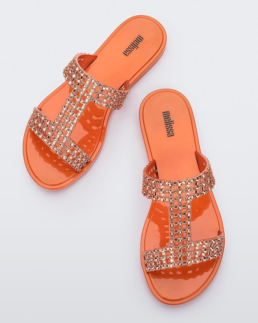 Top view of a pair of orange / copper Melissa Glowing slide with copper gem stones on the straps and an orange sole.