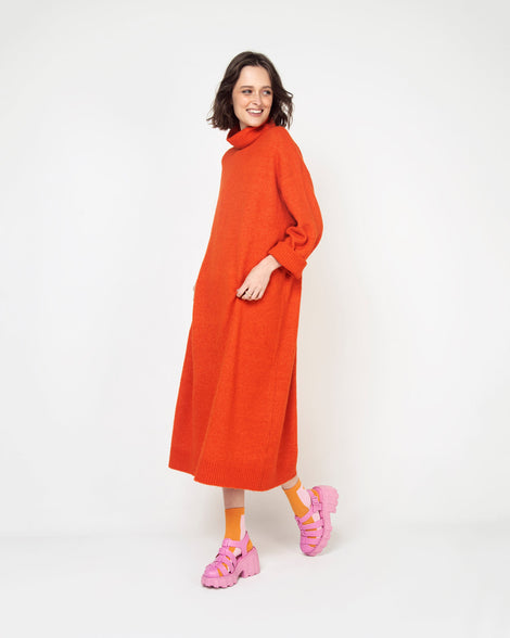 A woman in an orange dress wearing a pair of pink Melissa Megan planform heel sandals with socks.