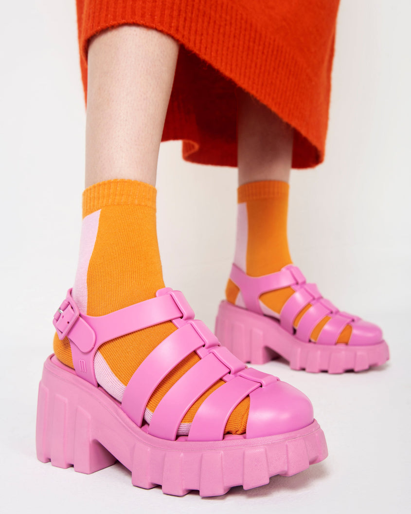A model's legs wearing a pair of pink Melissa Megan platform heels sandals with socks.