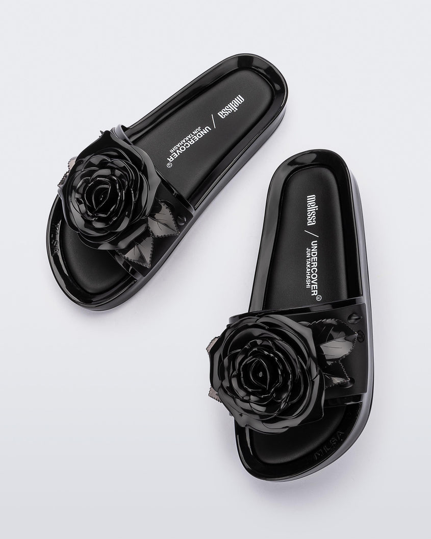 A top view of a pair of black Melissa Spikes Beach slides with a flower detail and spikes on the front strap.