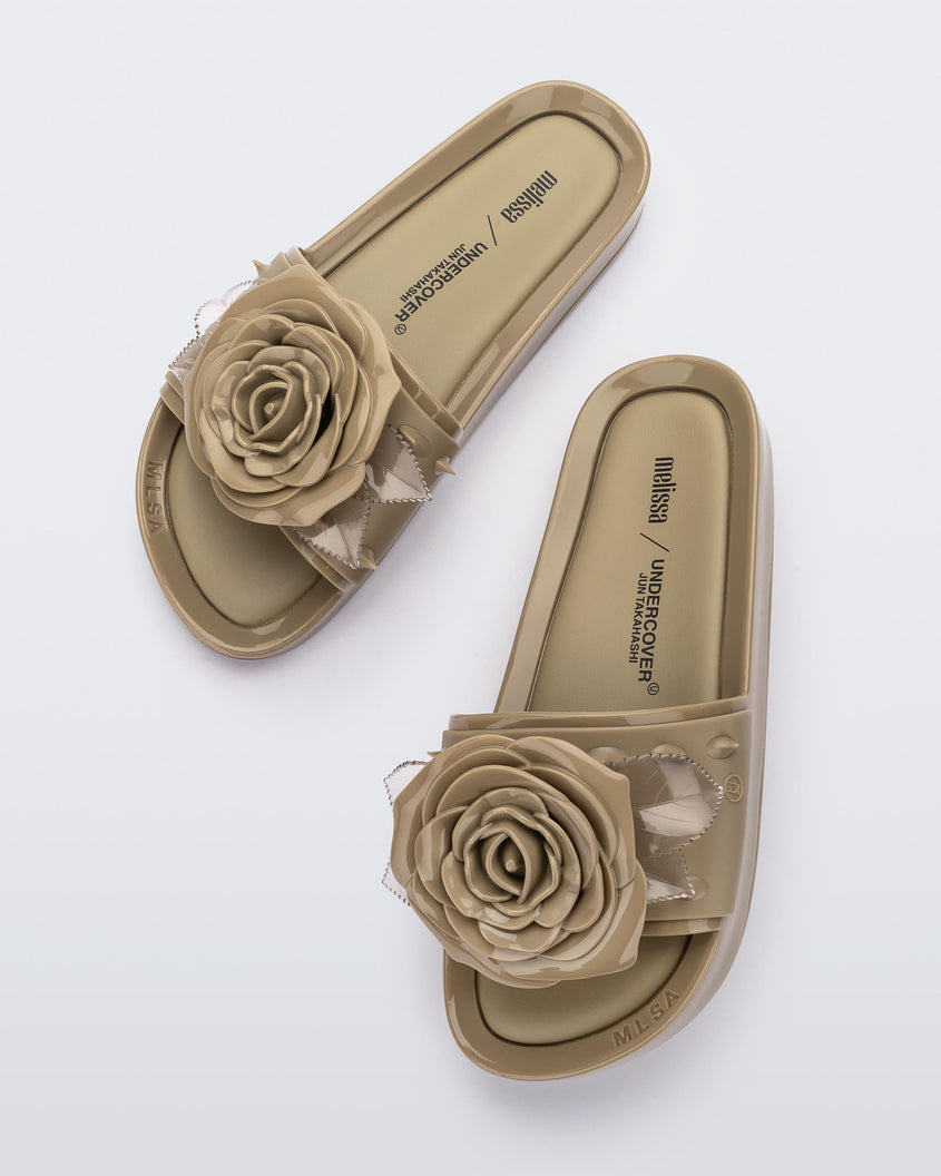 Top view of a pair of beige Melissa Spikes Beach slides with a flower detail and spikes on the front strap.