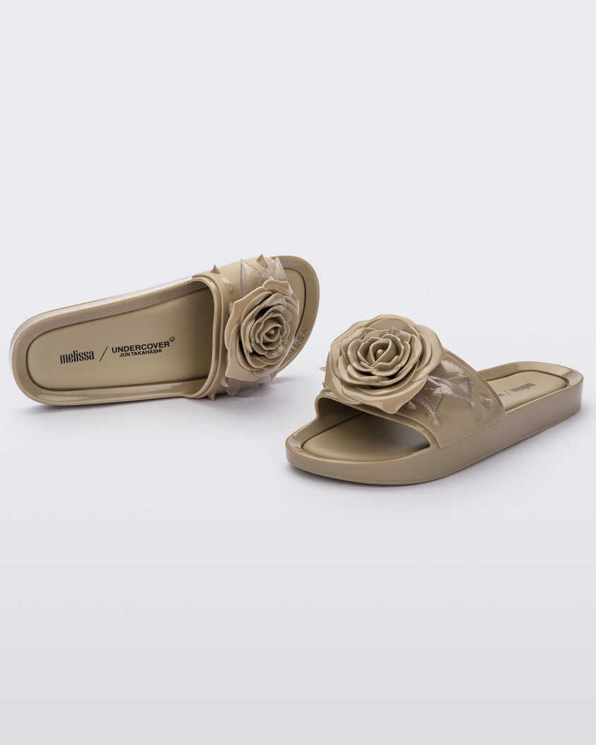 An angled front and top view of a pair of beige Melissa Spikes Beach slides with a flower detail and spikes on the front strap.
