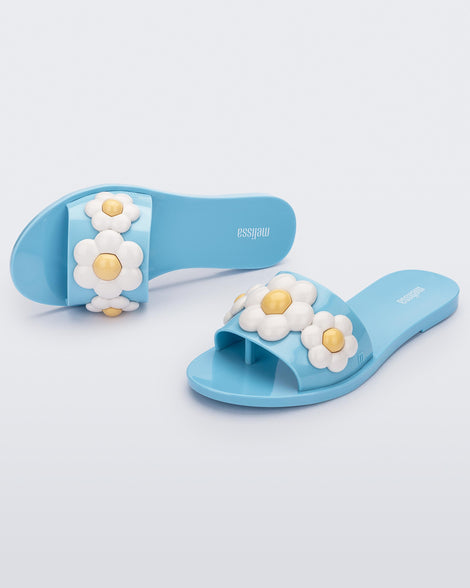 Top and angled view of a pair of blue Melissa Babe Spring slides with white flowers.