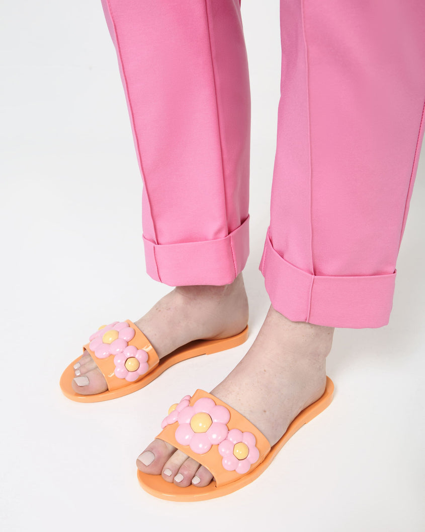 A model's legs wearing a pair of orange Babe Spring slides with pink flowers
