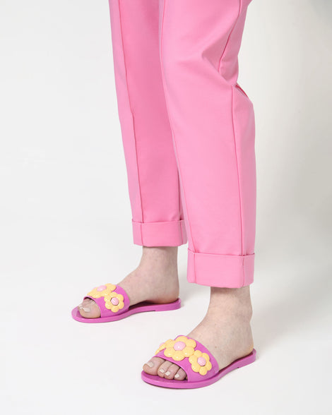 A mode's legs wearing a pare of pink Babe Spring Melissa slides with yellow flowers. 