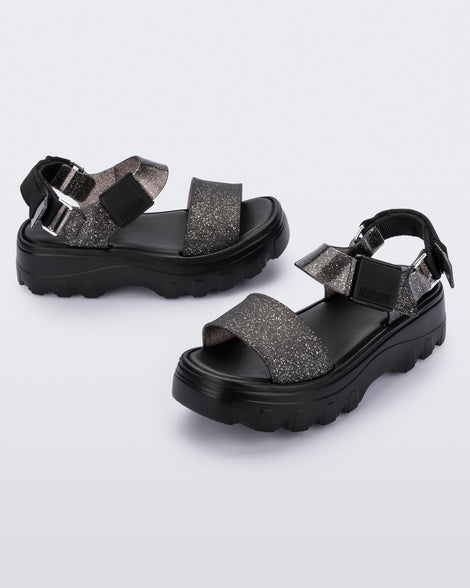 An angled top and side view of a pair of black/glitter black platform Melissa Kick Off Sandals with two glitter straps.