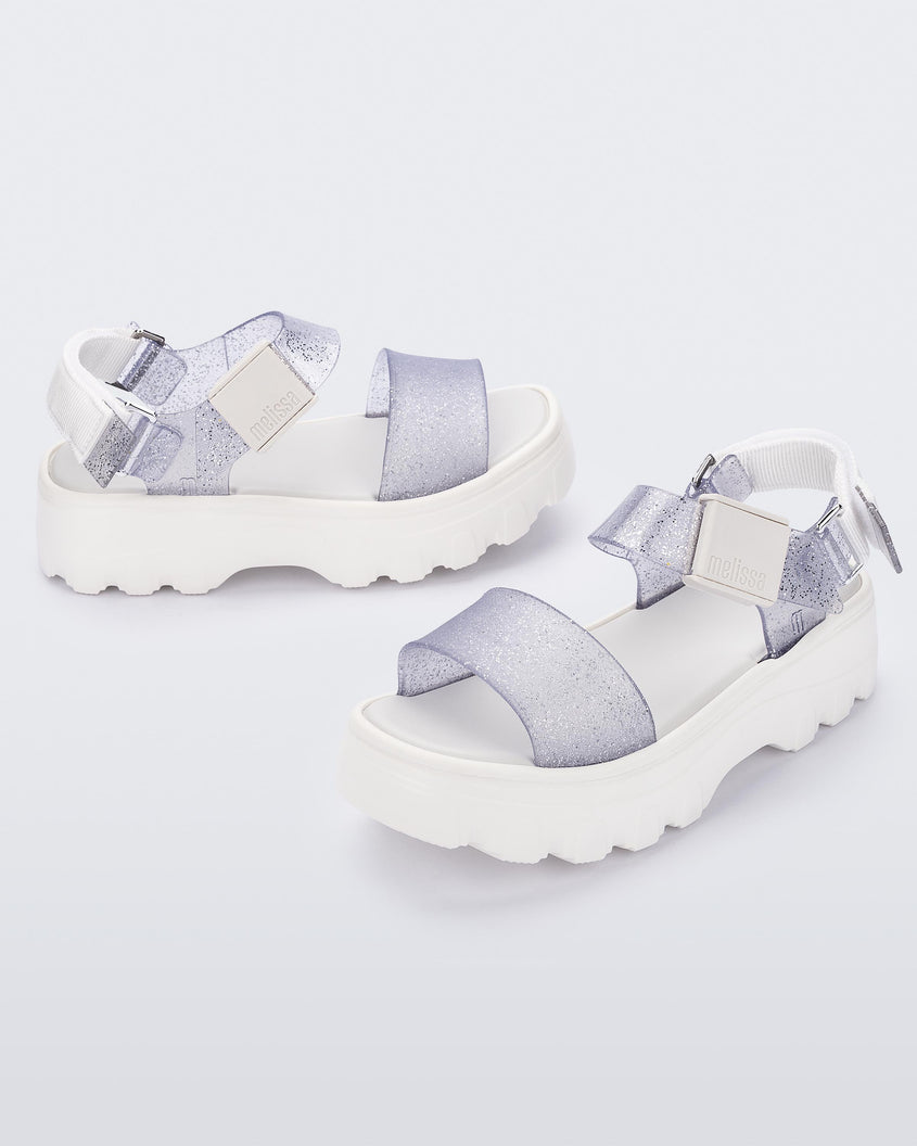 An angled top and side view of a pair of white/glitter clear platform Melissa Kick Off Sandals with two glitter straps.