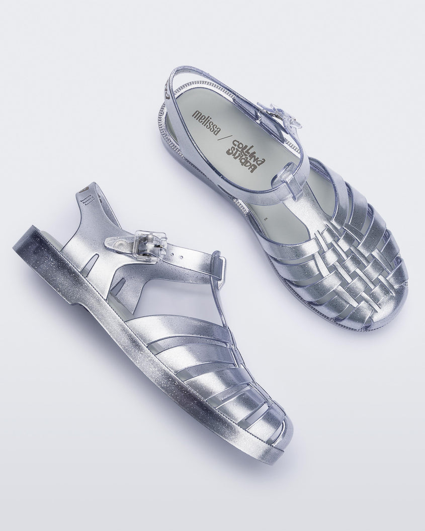 Top and side view of a pair of silver Melissa Possession sandals with a closed toe front weft design connected to a top strap with a buckle.